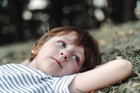 Kid lying on his back in the grass in park. Boy chilling on green lawn. Child relaxing outside, resting his head on garden meadow.の写真素材