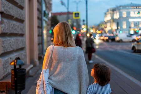 Mother and son walking in the city center street. Mom and kid taking a summer evening walk outside in the town. Family leisure time. City life.の写真素材