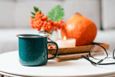 Still life book, candle, rowan berry, pumpkin and a cup of tea or coffee in the living room on a table, home decor in a cozy house. Autumn weekend concept, plaid. Fallen leaves and home decorationの写真素材