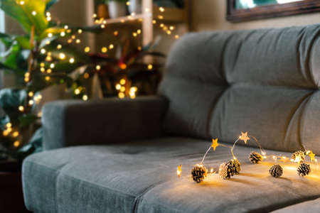 Christmas natural eco decoration, pine cone, lights on gray couch background at cozy home. Glowing light bokeh, coniferous branch. Winter holidays. Zero waste, plastic free. Indoors plantsの写真素材