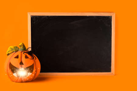 Halloween holiday concept. Jack o lantern with light bokeh, spider and blank frame chalkboard on orange background. Halloween festival party, greeting card with mockup copy space.の写真素材