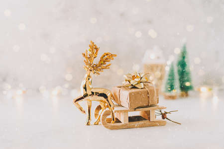 Golden deer dragging Natural Christmas gift on toy wooden sled on white background with glowing light bokeh, copy space. New year card. Xmas decoration, Christmas treeの写真素材