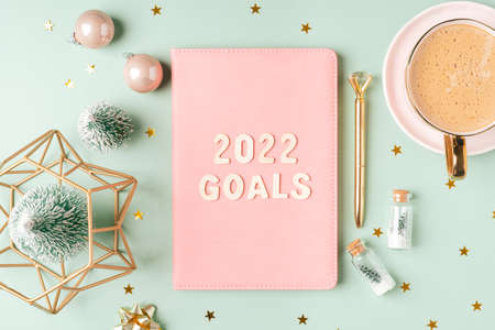 Top view Desktop Christmas pink notepad with 2022 goals letters text. Flat lay on green mint table background with planner, cup of coffee, candle, Christmas decoration, notebook and stationery.の写真素材