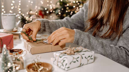 Woman s hands wrapping Christmas gift boxes, close up. Unprepared presents on white table with decor elements and items Christmas or New year DIY packing Concept.の写真素材