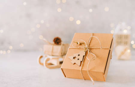 Eco Natural Christmas gift with wooden label tag on white background with glowing light bokeh, copy space. New year card. Xmas decoration with house. Zero waste conceptの写真素材