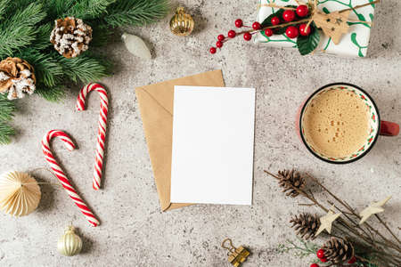 Flat lay of Mockup blank paper for Christmas greeting card. Gray background with cup of coffee, fir...
