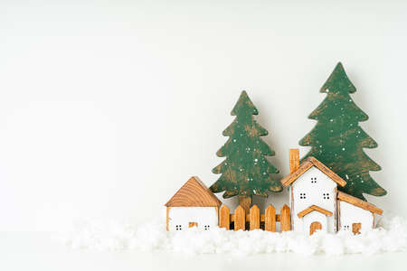 Happy New Year and Merry Christmas postcard. Festive white background with toy wooden house, snow, rustic christmas tree, village and decoration. Copy space for winter holidays greeting card.の写真素材
