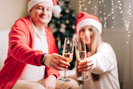 Family couple man and woman holding champagne glasses, close up. Celebrate New year after Christmas holidays. Home decor with Christmas tree.の写真素材