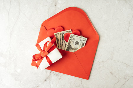 Red paper envelope with money dollars bills. Flat lay of gray working table background with Valentine gift, letter, heart shape. Top view, mock up greeting card. Valentines Day budgetの写真素材