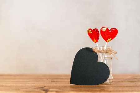 Still life Valentines day festive background with empty black chalkboard heart and 2 lollipop on...