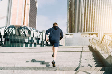 Young athlete man runner running up and down on city stairs in summer on morning run, background urban city street. Sports training. Fitness cardio workout in fresh air, walk outside.の写真素材