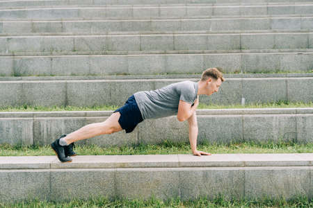 Young man has fitness workout. Male athlete does abs exercise, sport and training outdoor and stands...