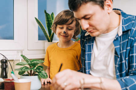 Easter day. Male Father and son painting eggs on wooden background. Family sitting in a kitchen....