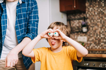 Easter day with kid. Father and son with funny face and eggs eyes, having fun together. Family man and child in a kitchen. Preparing for Easter, creative homemade decoration.の写真素材