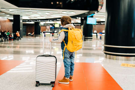 Child boy with backpack standing in the airport terminal, waiting for flight, travel with suitcase. Vacation concept.の写真素材