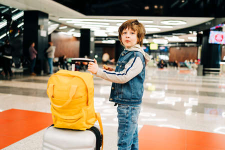 Child boy with backpack standing in the airport terminal, waiting for flight, travel with suitcase. Vacation concept.の写真素材