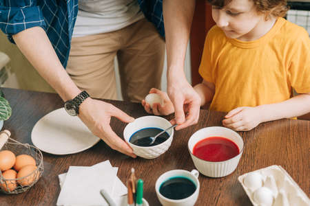 Easter day. Male Father and son painting eggs on wooden background. Family sitting in a kitchen. Preparing for Easter, creative homemade decoration. Child kid boy having fun and painting easter eggsの写真素材