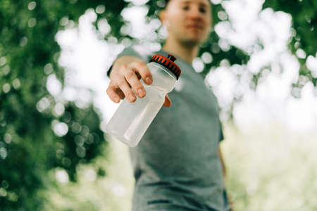 Close up of Young man runner in hoodie Holding water bottle while doing workout in summer sunny...