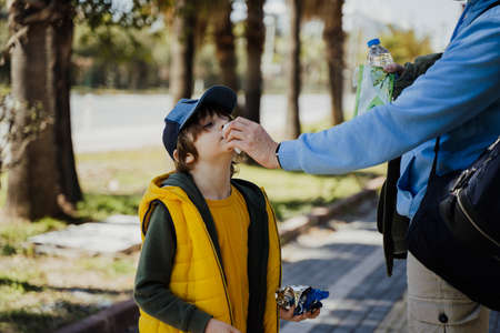 Father helps little son to blow his nose with the nandkerchief. Dad wiping boys nose with disposable paper napkin. Schoolboy gets his nose cleaned with tissue by fathers handの写真素材