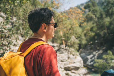 Close-up rear view of adult male tourist walking a stone footpath in spring forest. Young guy wearing casual clothes and yellow backpack while hiking in summer greenwood forest.の写真素材