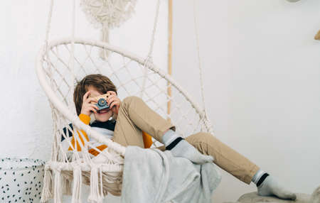 Smiling caucasian little Cute preschooler child boy having fun and playing with toy camera. Kid acting like a professional photographer taking photos at home in kids room. Background with copy spaceの写真素材