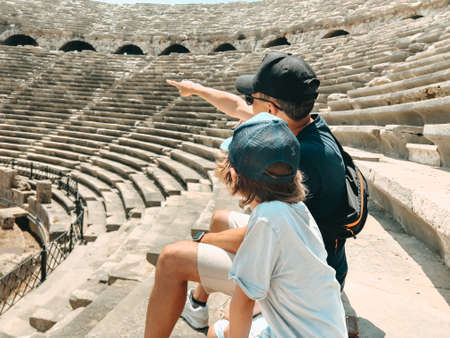 Young father dad and his school boy kid son tourists visiting ancient antique coliseum amphitheater ruins in hot summer day.の写真素材