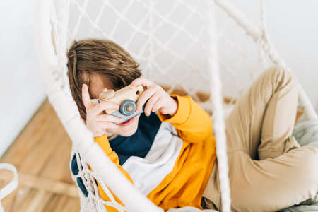 Smiling caucasian little Cute preschooler child boy having fun and playing with toy camera. Kid acting like a professional photographer taking photos at home in kids room. Background with copy spaceの写真素材