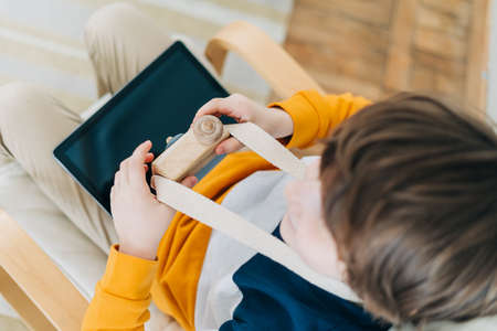 Caucasian little Cute preschooler child boy having fun and playing with tablet and toy wooden camera. Kid acting like a professional photographer taking photos at home in kids room.の写真素材