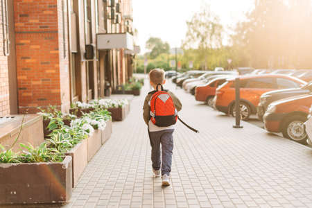 Back to school. Cute child with backpack going to school. Boy pupil with bag. Elementary school student going to classes. Kid walking outdoors on the city street after class. Back viewの写真素材
