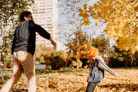 Father and son having fun in autumn park with fallen leaves, throwing up leaf. Child kid boy and his dad outdoors playing with maple leavesの写真素材