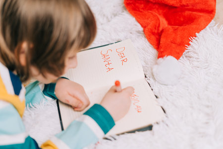 Close up hands of Kid boy, lying on couch and writing letter in note pad to dear Santa at home in Christmas holidays. Child wish list. Dreams of a Christmas gifts. Merry Christmas and Happy new yearの写真素材