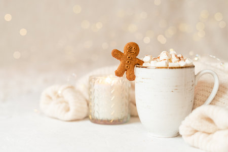 Gingerbread man cookie in cup of hot cocoa or coffee with marshmallow, candle, cinnamon and warm cozy sweater. Christmas lights background. Xmas holiday wooden star decorations.の写真素材