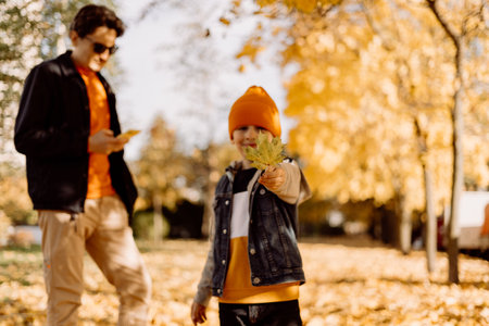 Father and son having fun in autumn park with fallen leaves, throwing up leaf. Child kid boy and his dad outdoors playing with maple leavesの写真素材