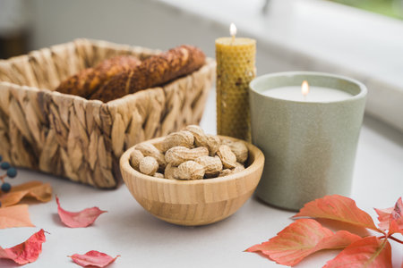 Still life candle flame, peanut, fallen leaves, wicker basket, bagel on a table, home decor in a...