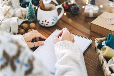 Woman hand holding pen on notepad at home on winter holidays xmas. Goals plans make to do and wish list for new year christmas concept, girl writing in notebook. Christmas decoration, gift boxes.の写真素材