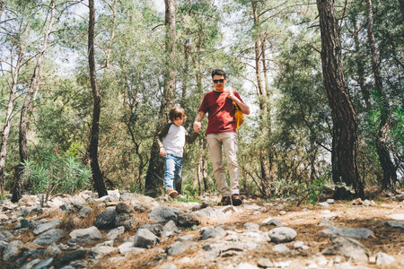Tourists school boy and his dad walking in the spring forest. Child boy and father wearing casual clothes hiking in summer greenwood leaf forest. Family adventure in the woods.の写真素材