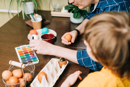 Easter day. Male Father and son painting eggs on wooden background. Family sitting in a kitchen. Preparing for Easter, creative homemade decoration. Child kid boy having fun and painting easter eggsの写真素材