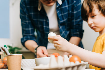 Easter day. Male Father and son painting eggs on wooden background. Family sitting in a kitchen. Preparing for Easter, creative homemade decoration. Child kid boy having fun and painting easter eggsの写真素材