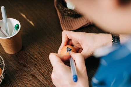 Easter day. Cropped hands of Adult man painting eggs on wooden background. Sitting in a kitchen with...