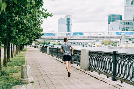Young athlete man runner running at summer morning, background urban city street. Sports training. Fitness cardio workout in fresh air, jogging outside.の写真素材