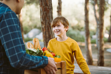 Father and son farmers holding a wooden crate with supplies groceries. Man male dad and his should kid boy child delivered a framed box with organic vegetables and bread to farmers marketの写真素材