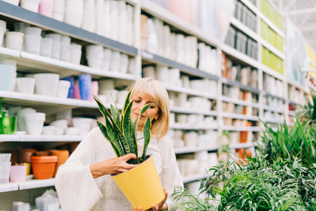 Gardening, planting and shopping concept. Beautiful mature adult woman choosing houseplants and pots in greenhouse or garden centre. Senior buying flowers plants at market store in mall.の写真素材
