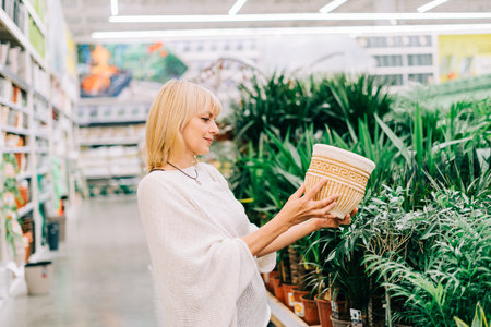 Gardening, planting and shopping concept. Beautiful mature adult woman choosing houseplants and pots in greenhouse or garden centre. Senior buying flowers plants at market store in mall.の写真素材