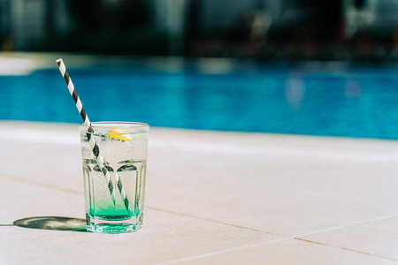 The glass of sparkling mint fruit cocktail standing by the swimming pool. Summer alcohol free drink by the hotel pool. Hello summer holiday vacation.の写真素材