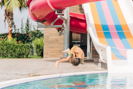Child jumping and dives in swimming pool at sunny day. Kid boy refreshing and playing at heat weather, active vacation and healthy lifestyle. Happy summer.の写真素材