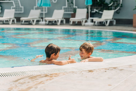 Two brothers Childs laughing while playing in swimming pool at sunny day. Kids friends boys refreshing at heat weather, active vacation and healthy lifestyle. Happy summer.の写真素材