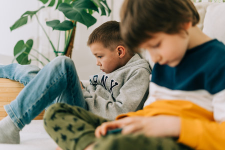 Cheerful two brothers boys playing online game, watching video on cellphone. Smiling kids using funny mobile apps, enjoying free leisure time at home on couch. Children texting together at phone.の写真素材