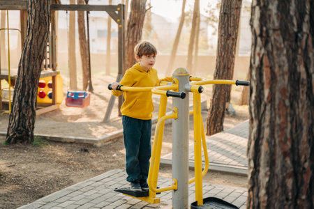 Elementary school boy using fitness exercise equipment in the public city park. Kid playing standing doing exercises on workout equipment in the forest park.の写真素材