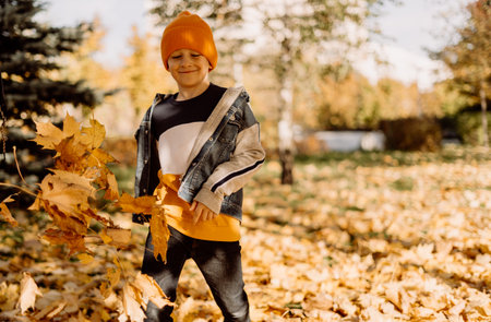 Kid having fun in autumn park with fallen leaves, throwing up leaf. Child boy outdoors playing with maple leavesの写真素材