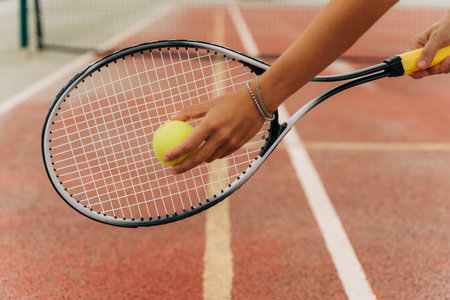 Closeup picture of attractive sporty woman hands holding yellow tennis ball and racket with tennis net and synthetic hard tennis court on the background.の写真素材